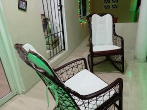 Un pasillo con una silla, una mesa, una ventana con barrotes y una tira decorativa de luces.