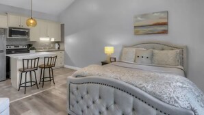 Una camera da letto moderna con un letto grande, una zona pranzo separata con sgabelli da bar e una cucina con forno a microonde e fornelli.
