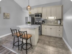A kitchen with a central island, white cabinets, stainless steel appliances, and two bar stools. - Stylish ParkCity Boutique studio with effortless access to slopes +Free Parking (Park City)