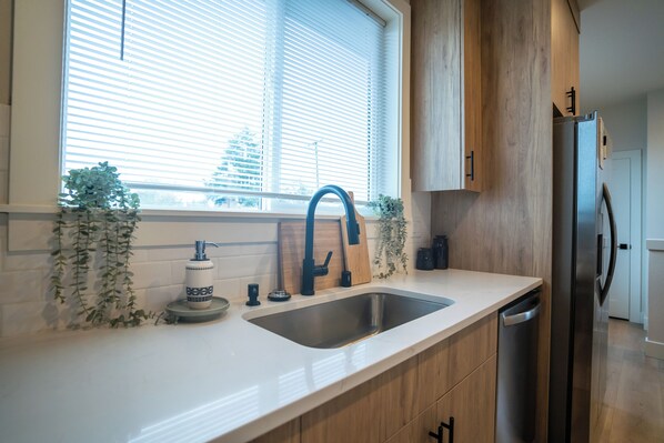 A kitchen with a stainless steel sink, wooden cabinets, and a built-in dishwasher.