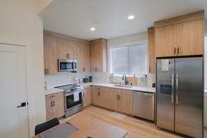 A modern kitchen with wooden cabinets, stainless steel appliances, a built-in microwave, and a window with blinds. - Luxury Home in Heart of Vancouver / Quiet & Cozy (Vancouver)