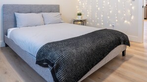 Ett modernt sovrum med en stor säng, en grå sänggavel och en ljusslinga på väggen.