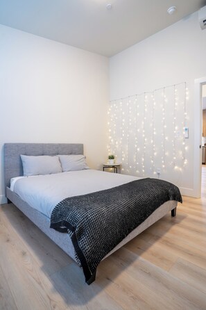 A modern bedroom with a large bed, a grey headboard, and a string of lights on the wall. - Luxury Home in Heart of Vancouver / Quiet & Cozy (Vancouver)