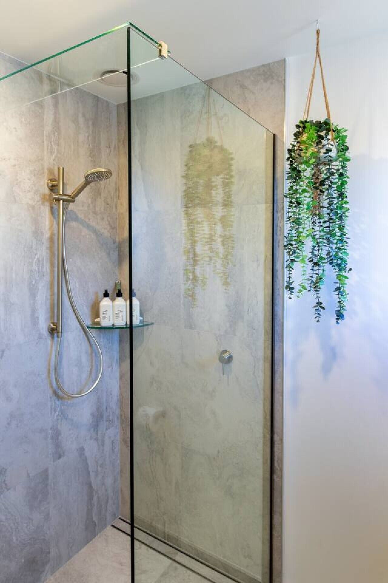 Ducha moderna con cabina de vidrio, cabezal de ducha de mano y estante con artículos de aseo.