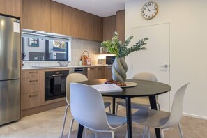 A modern kitchen with wooden cabinets, stainless steel appliances, a dining table with chairs, and a clock on the wall. - City Fringe 2BR 2BA Townhouse | Parking + EV (Christchurch)