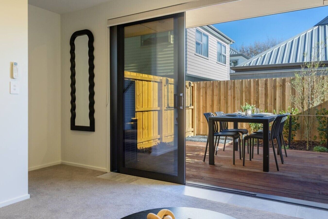 A room with a sliding glass door leading to an outdoor patio with a wooden deck, a dining table, and chairs.