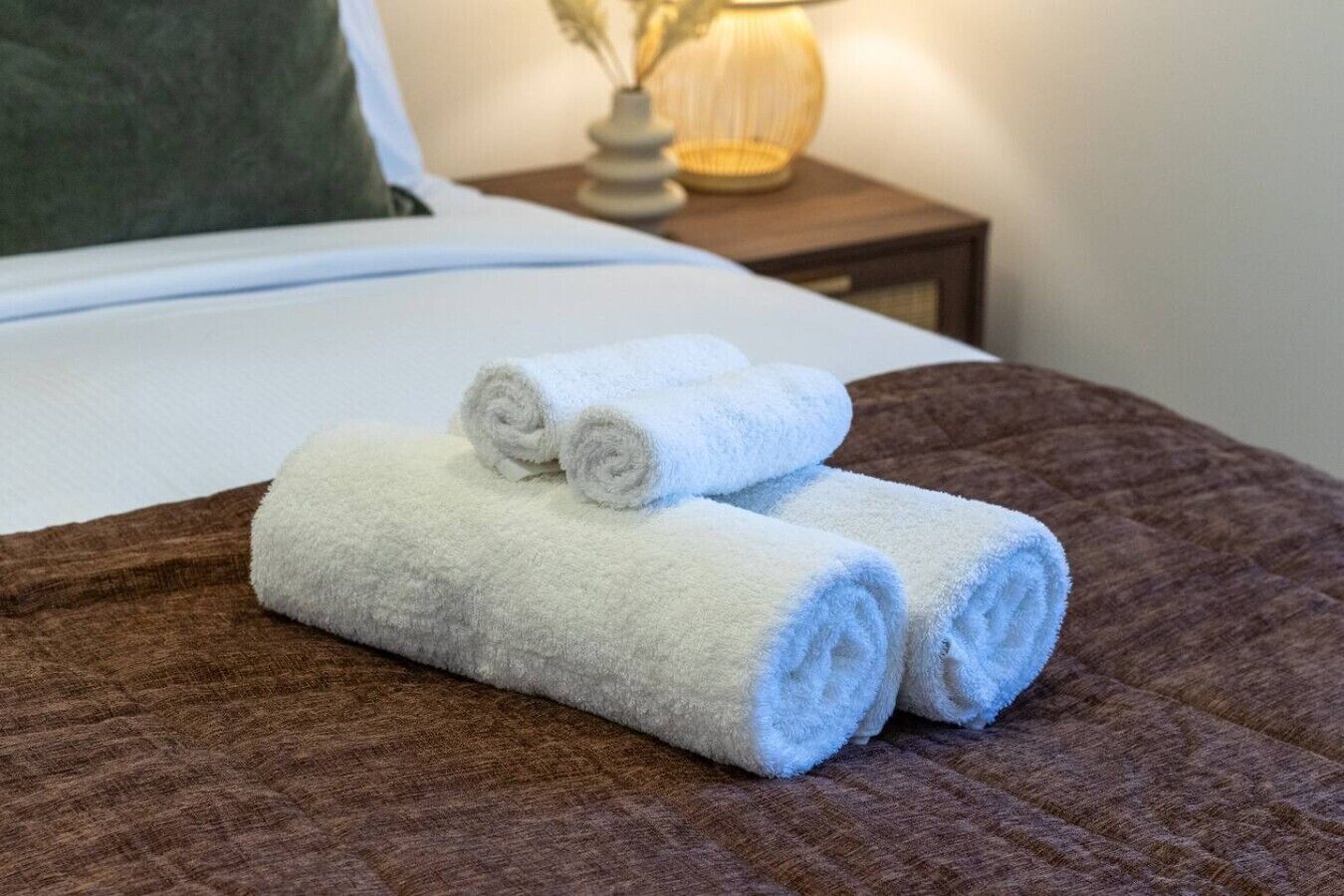 Ein Bett mit einer braunen Steude und zwei aufgerollten weißen Handtüchern darauf.