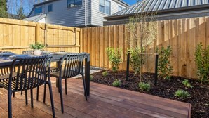 A wooden deck with a table and chairs, surrounded by a wooden fence and small plants. - City Fringe 2BR 2BA Townhouse | Parking + EV (Christchurch)