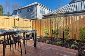 Eine Holzterrasse mit Tisch und Stühlen, umgeben von einem Holenzaun und kleinen Pflanzen.