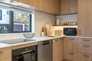 A modern kitchen with wooden cabinets, a dishwasher, a built-in oven, and a window with a view of the outside. - City Fringe 2BR 2BA Townhouse | Parking + EV (Christchurch)