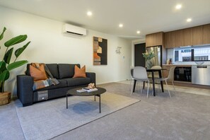 A modern living room with a sofa, coffee table, and a dining area with chairs. - City Fringe 2BR 2BA Townhouse | Parking + EV (Christchurch)