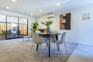 Uma sala de jantar moderna com uma mesa redonda, cadeiras cinzas, um vaso com plantas e um quadro contemporâneo na parede.
