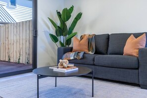 A modern living room with a grey sofa, a round black coffee table, and a large green plant. - City Fringe 2BR 2BA Townhouse | Parking + EV (Christchurch)
