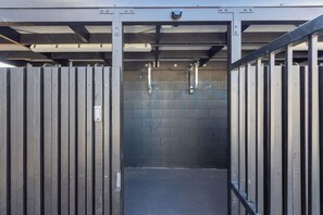 A metal gate leading to a covered area with a brick wall and a hose reel. - City Fringe 2BR 2BA Townhouse | Parking + EV (Christchurch)
