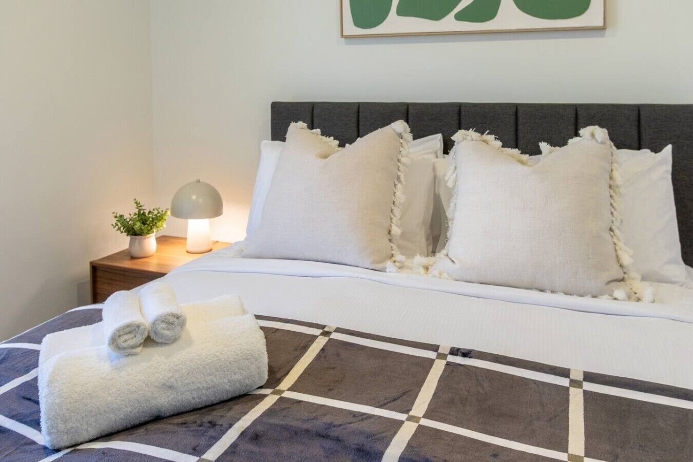 A neatly made bed with a grey headboard, white pillows, and a checkered bedspread.