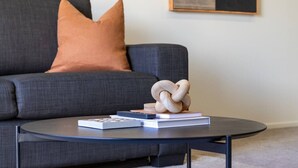 A modern living room with a dark grey sofa, a round coffee table, and a wooden sculpture. - City Fringe 2BR 2BA Townhouse | Parking + EV (Christchurch)