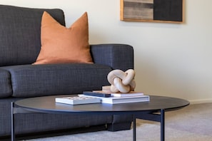 Ein modernes Wohnzimmer mit einem dunkelgrauen Sofa, einem runden Couchtisch und einer Holzskulptur.