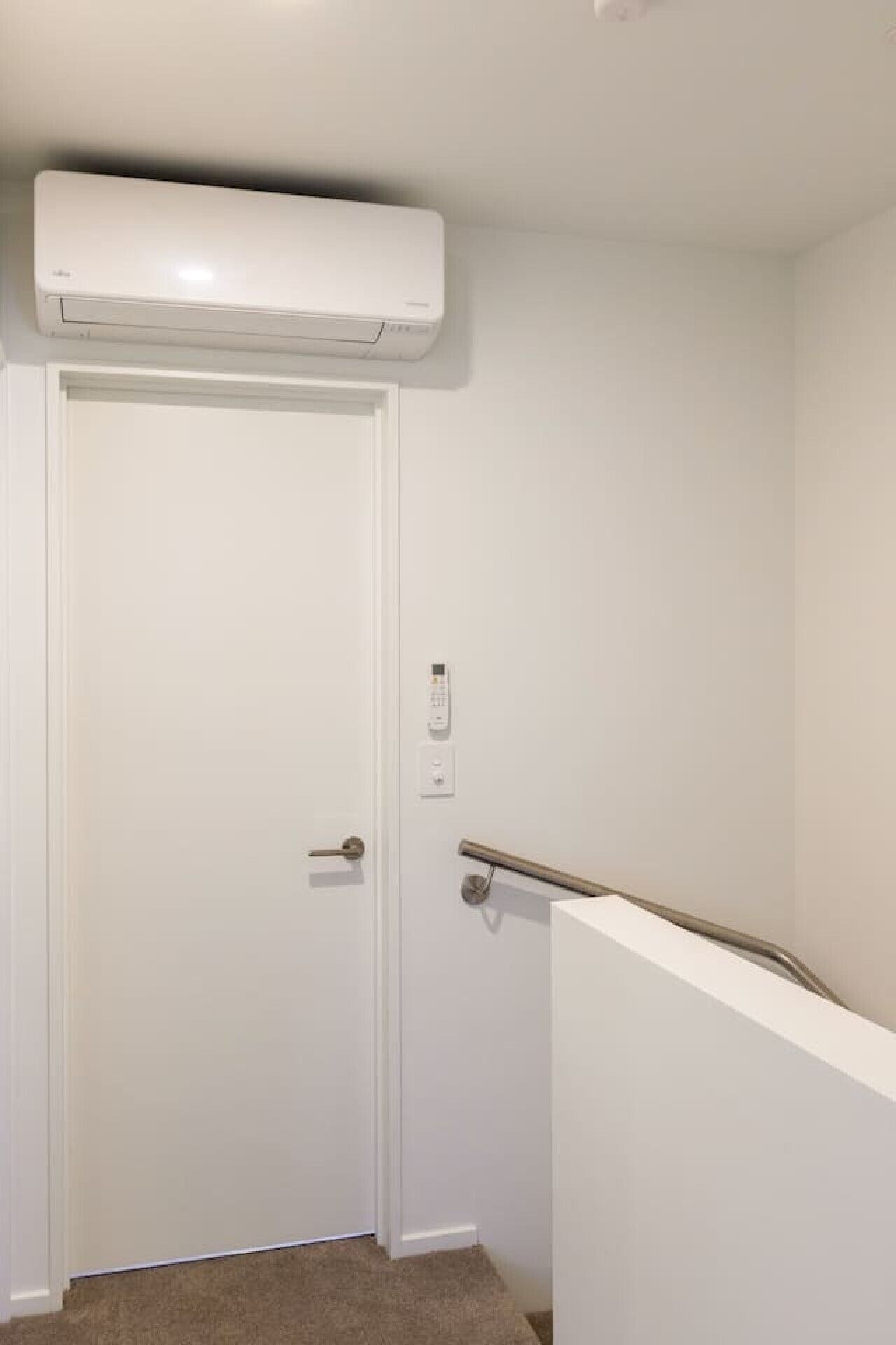 A white door with a handle, a wall-mounted air conditioning unit above it, and a handrail on the right side.