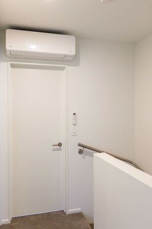 A white door with a handle, a wall-mounted air conditioning unit above it, and a handrail on the right side. - City Fringe 2BR 2BA Townhouse | Parking + EV (Christchurch)
