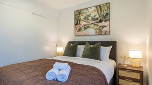 A hotel room with a bed, pillows, a painting, and a nightstand with a lamp. - City Fringe 2BR 2BA Townhouse | Parking + EV (Christchurch)