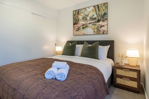 Ein Hotelzimmer mit einem Bett, Kissen, einem Gemälde und einem Nachttisch mit Lampe.