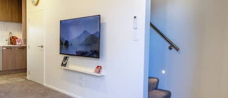 Una sala de estar con un televisor montado en la pared, un estante con objetos, un reloj y una escalera.
