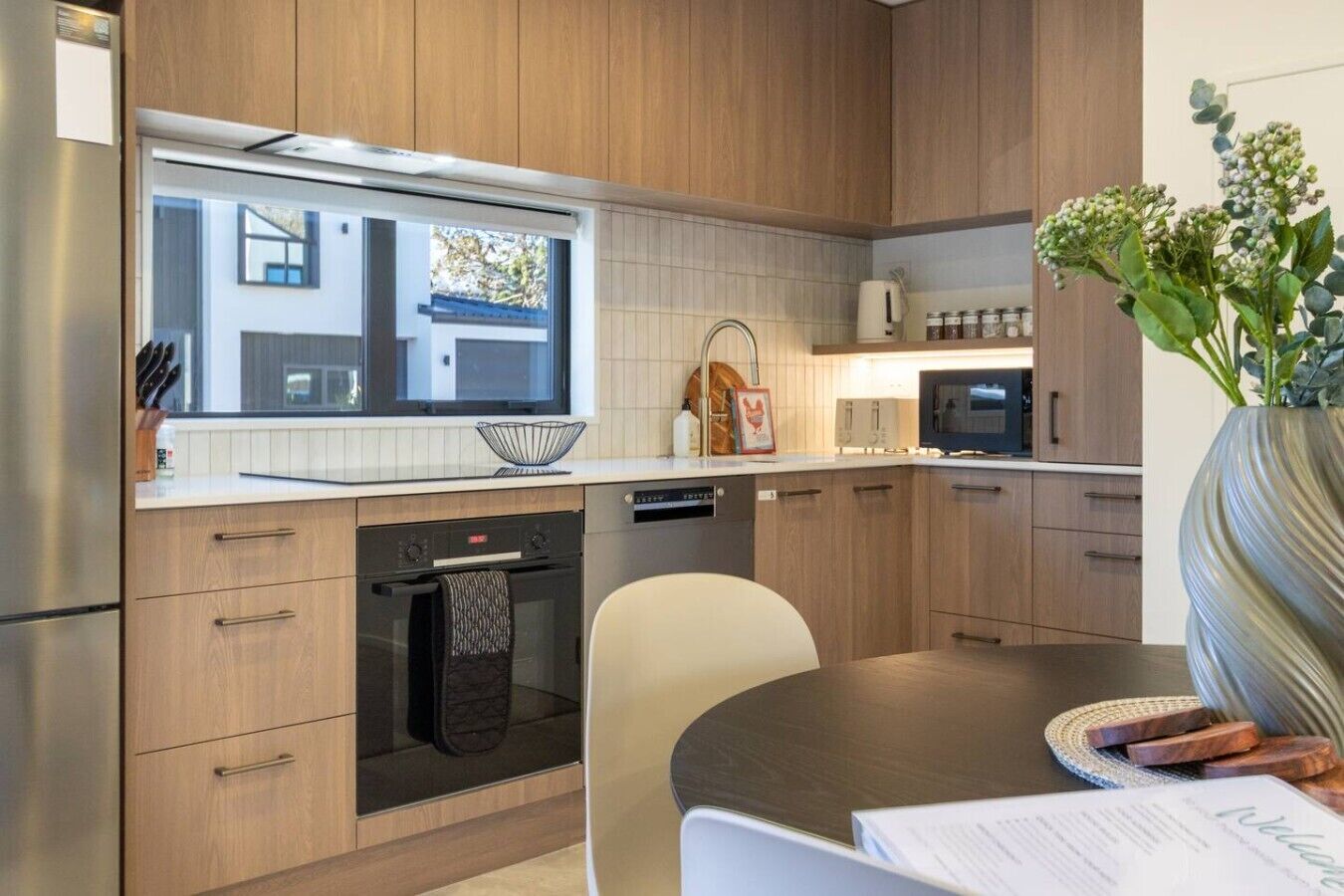 A modern kitchen with wooden cabinets, a built-in oven, and a dining area with a table and chairs.