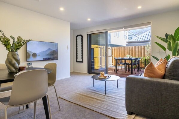 Uma sala de estar moderna com um sofá, cadeiras, uma mesa de centro, uma televisão e um espaço de jantar com mesa e cadeiras.