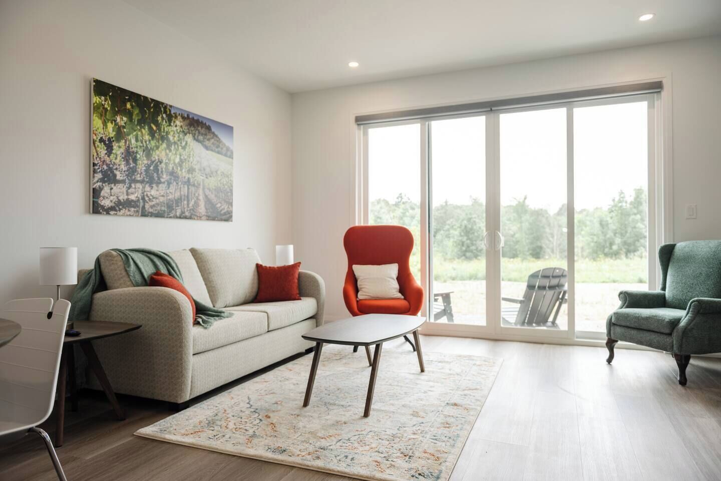 Ein modernes Wohnzimmer mit einer Couch, zwei Sesseln, einem Couchtisch und einem großen Fenster mit Blick auf Grünflächen.