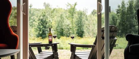 A room with a large sliding glass door leading to an outdoor area with two chairs and a table, a bottle of wine, and two glasses on the table.
