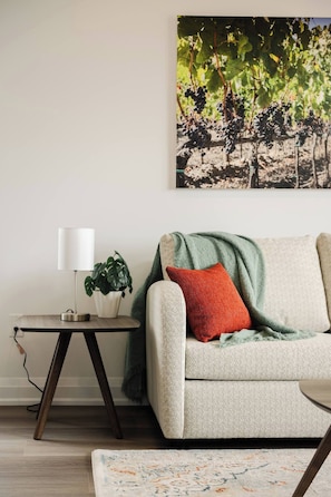 En stue med sofa, lampe, plante og et billede på væggen.