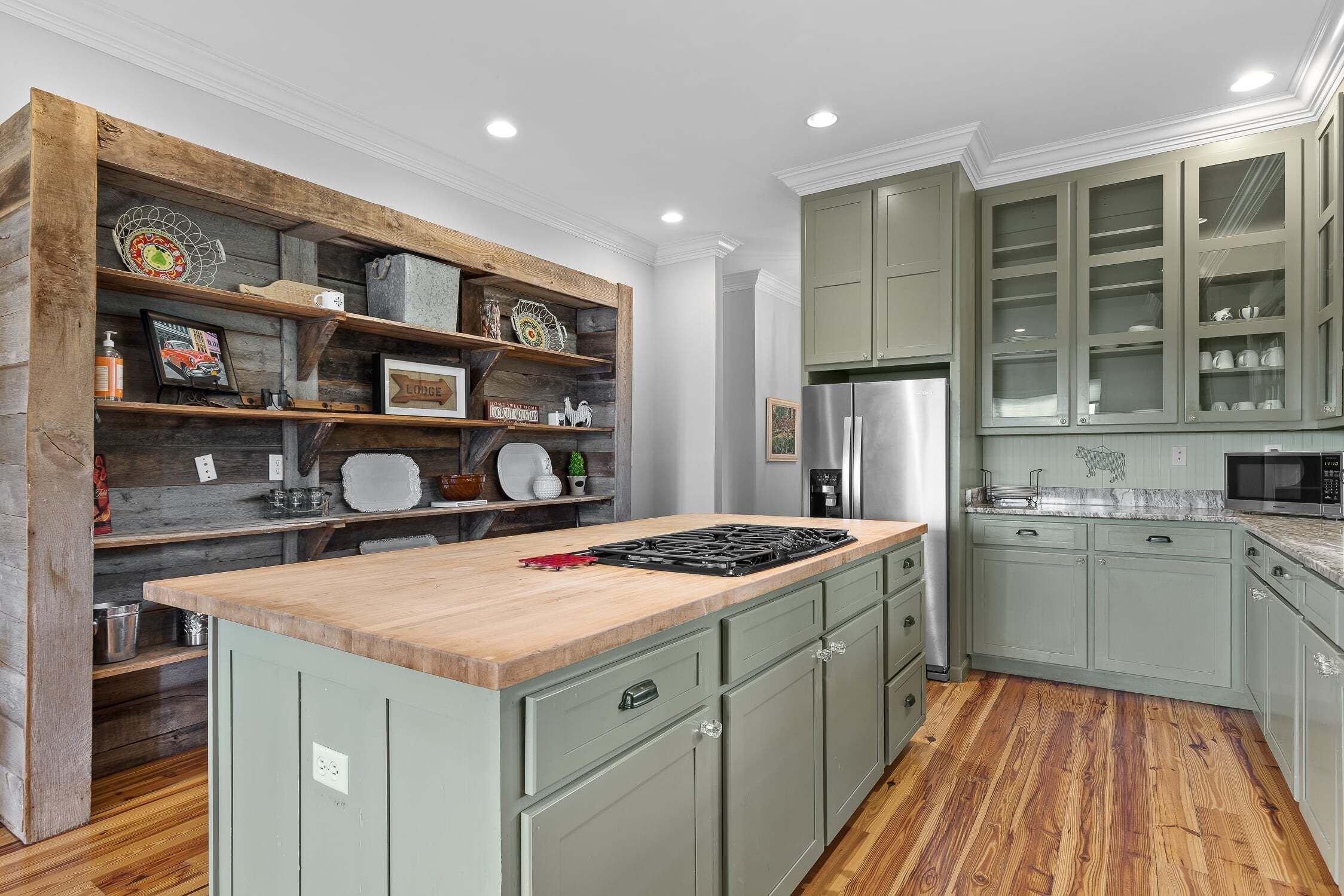 Una cocina moderna con estantes de madera, estufa integrada y gabinetes verdes.