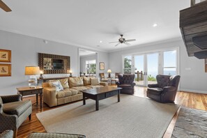 A spacious living room with a fireplace, a ceiling fan, and a large window offering a view of the outdoors. - McLemore Resort - 856 Canyon Ridge Road - French Country Home - Walking distance to Range and Clubhouse (Rising Fawn)