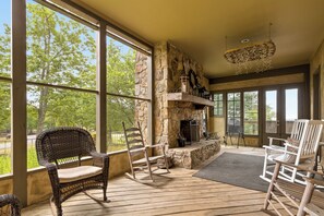 A spacious porch with wicker chairs, a stone fireplace, and large windows offering a view of trees. - McLemore Resort - 856 Canyon Ridge Road - French Country Home - Walking distance to Range and Clubhouse (Rising Fawn)