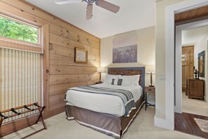Una camera da letto con pannello murale in legno, un letto con biancheria bianca, una ventola a soffitto e una finestra con persiane.