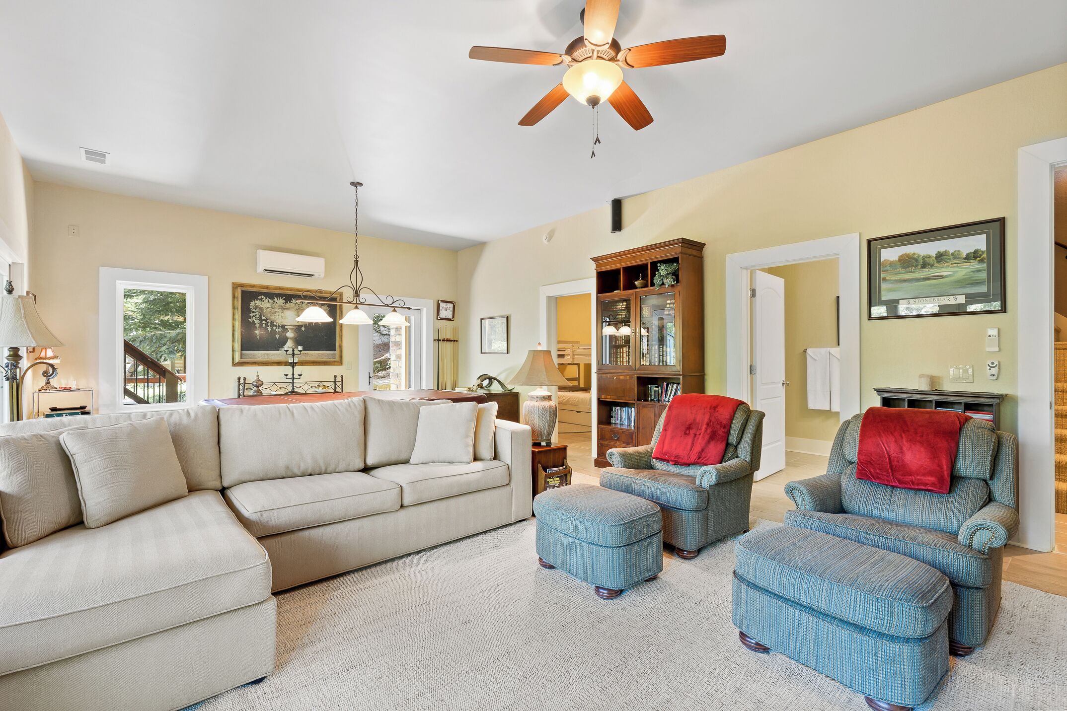 A spacious living room with a beige sofa, blue armchairs, and a wooden cabinet.