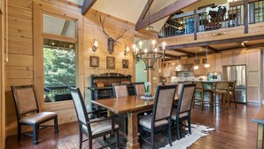 A spacious dining area with a wooden table and chairs, a chandelier, and a view of the outdoors. - McLemore Resort - 33 Eagle Creek Trail - Forest Cabin (Rising Fawn)
