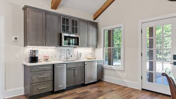 A kitchen with dark cabinets, a microwave, and a dishwasher. There is a window with a view of trees.