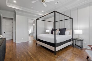 Ein Schlafzimmer mit Himmelbett, Nachttisch mit Lampe und Blick auf ein Badezimmer durch eine offene Tür.