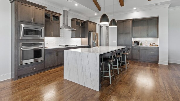 A modern kitchen with dark wood cabinetry, stainless steel appliances, and a marble island with bar stools. - McLemore Resort - 207 Rushing Water Trail - Golf Course View (Rising Fawn)