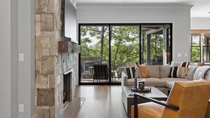 A modern living room with a stone fireplace, a large sofa, and a dining area. - McLemore Resort - 207 Rushing Water Trail - Golf Course View (Rising Fawn)