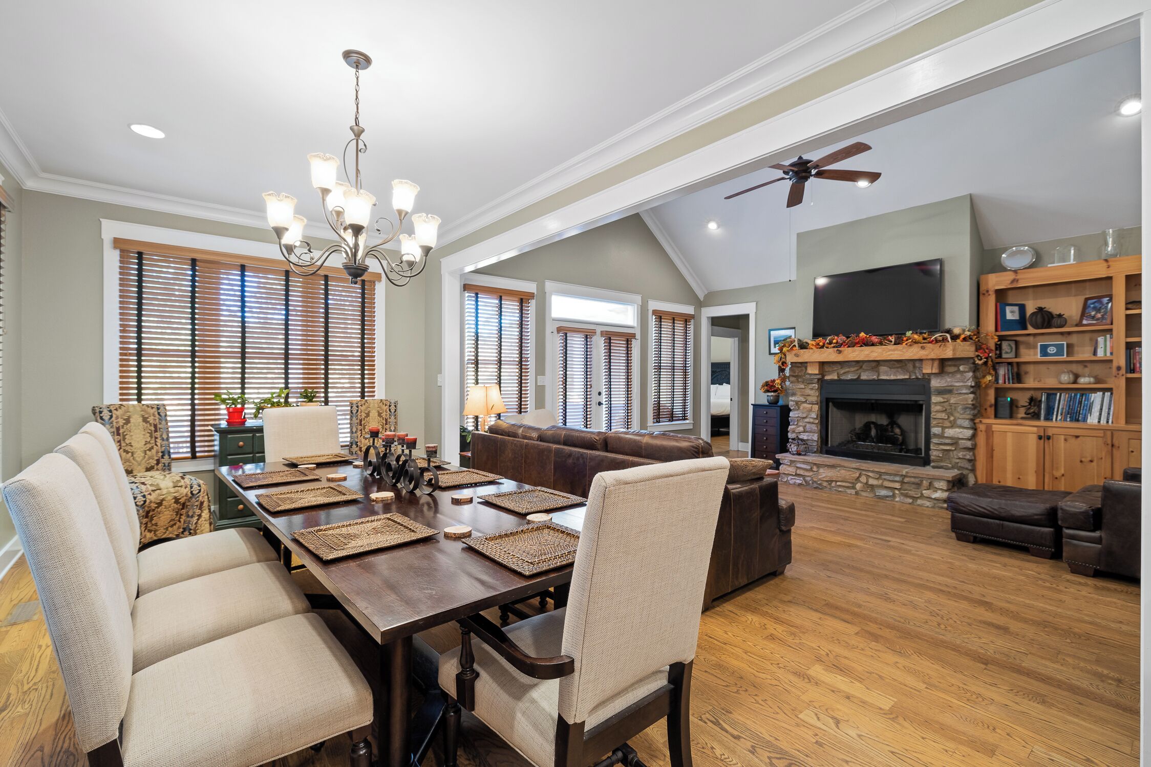 A spacious living room with a fireplace, a dining area with a chandelier, and a ceiling fan.