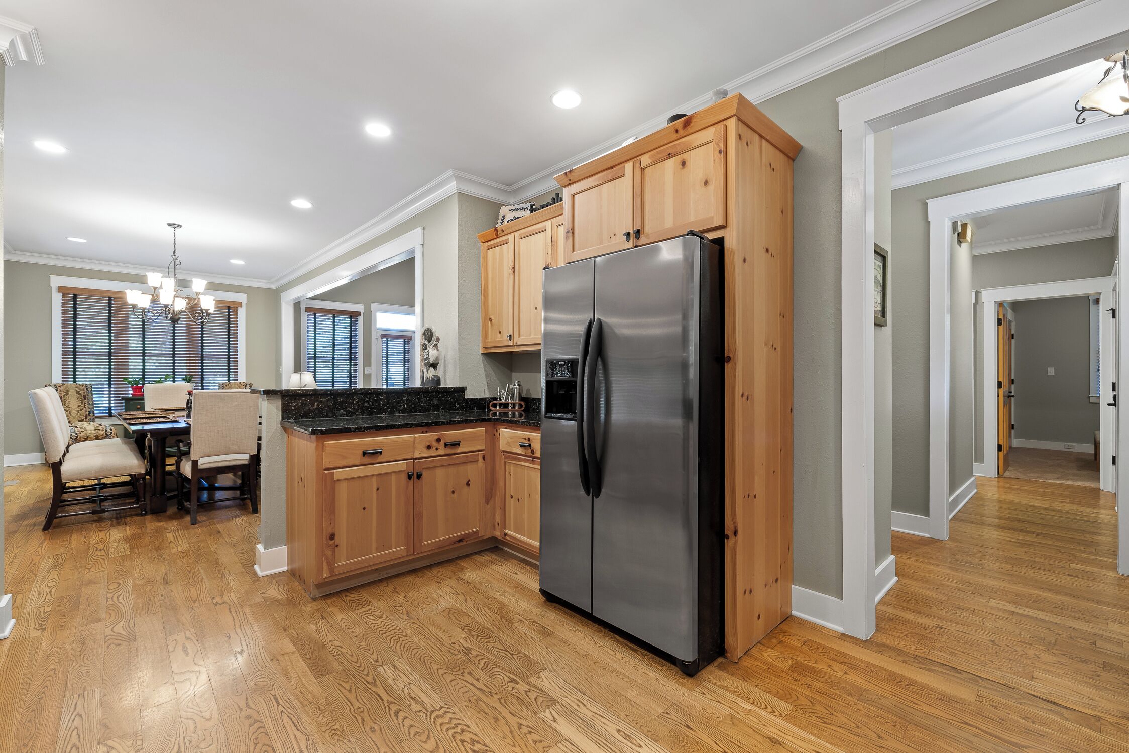 A modern kitchen with wooden cabinets, a stainless steel refrigerator, and a dining area with a table and chairs.
