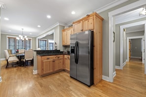 A modern kitchen with wooden cabinets, a stainless steel refrigerator, and a dining area with a table and chairs. - McLemore Resort - 19 Sunshine Trail  - Golf Course View (Rising Fawn)
