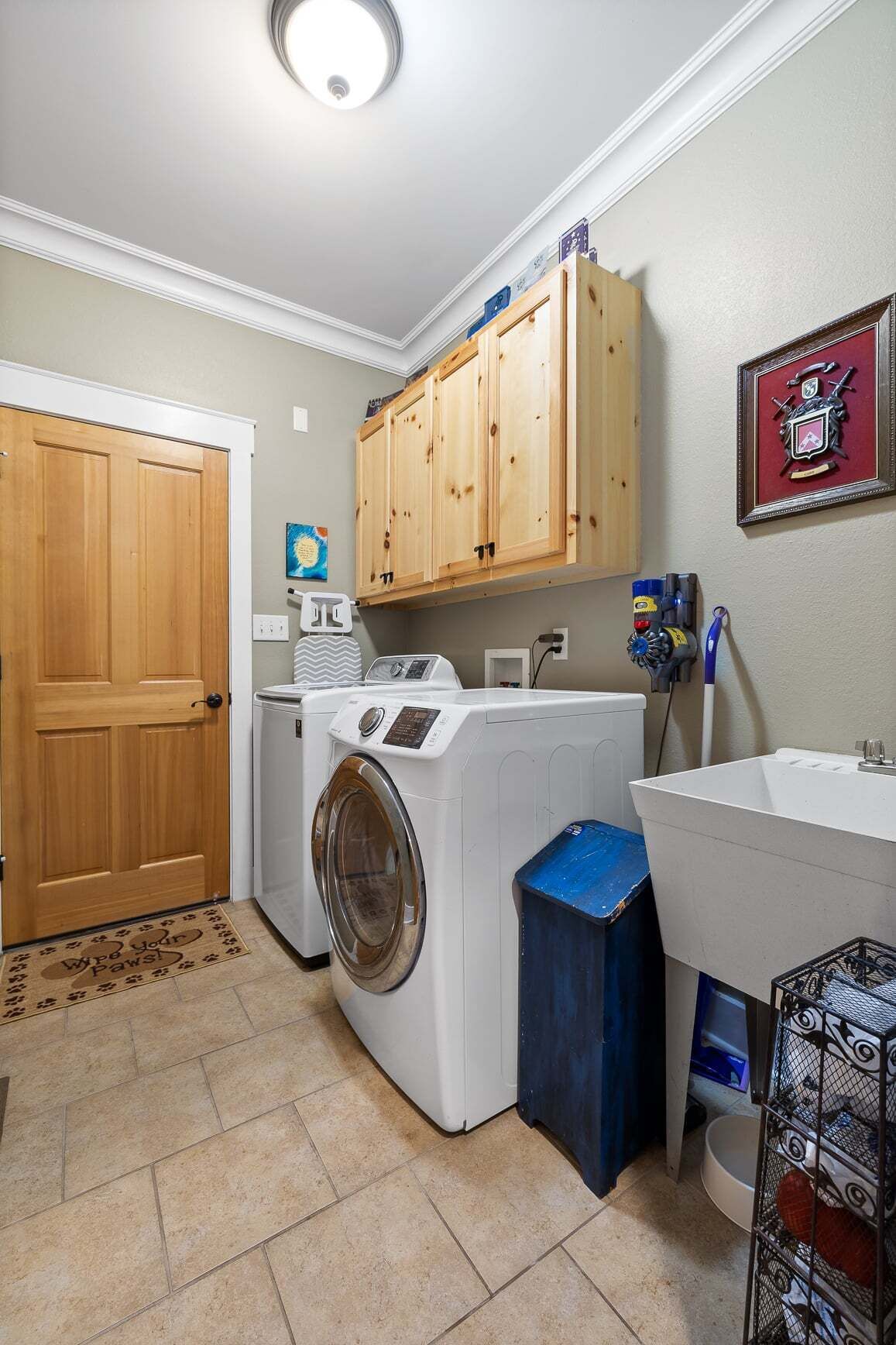 A laundry room with a washing machine, dryer, wooden cabinets, a sink, and a framed picture on the wall.