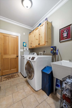 A laundry room with a washing machine, dryer, wooden cabinets, a sink, and a framed picture on the wall. - McLemore Resort - 19 Sunshine Trail  - Golf Course View (Rising Fawn)