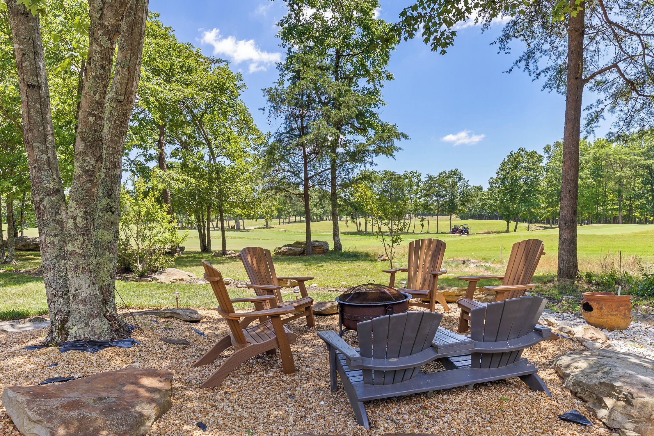 A seating area with Adirondack chairs, a fire pit, and a view of a golf course.