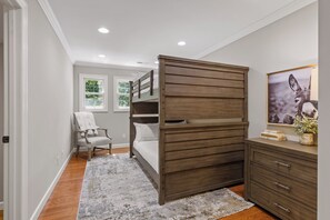 Ein Schlafzimmer mit Etagenbett, Stuhl, Kommode und Fenster.
