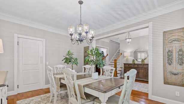 A dining room with a chandelier, white chairs, a wooden table, and a staircase in the background. - McLemore Resort - 454 Rushing Water Trail - Golf Course View (Rising Fawn)