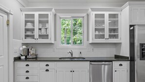 A kitchen with white cabinetry, a stainless steel dishwasher, and a window with a view of greenery. - McLemore Resort - 454 Rushing Water Trail - Golf Course View (Rising Fawn)